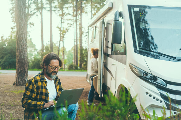 Man using laptop in nature next to RV