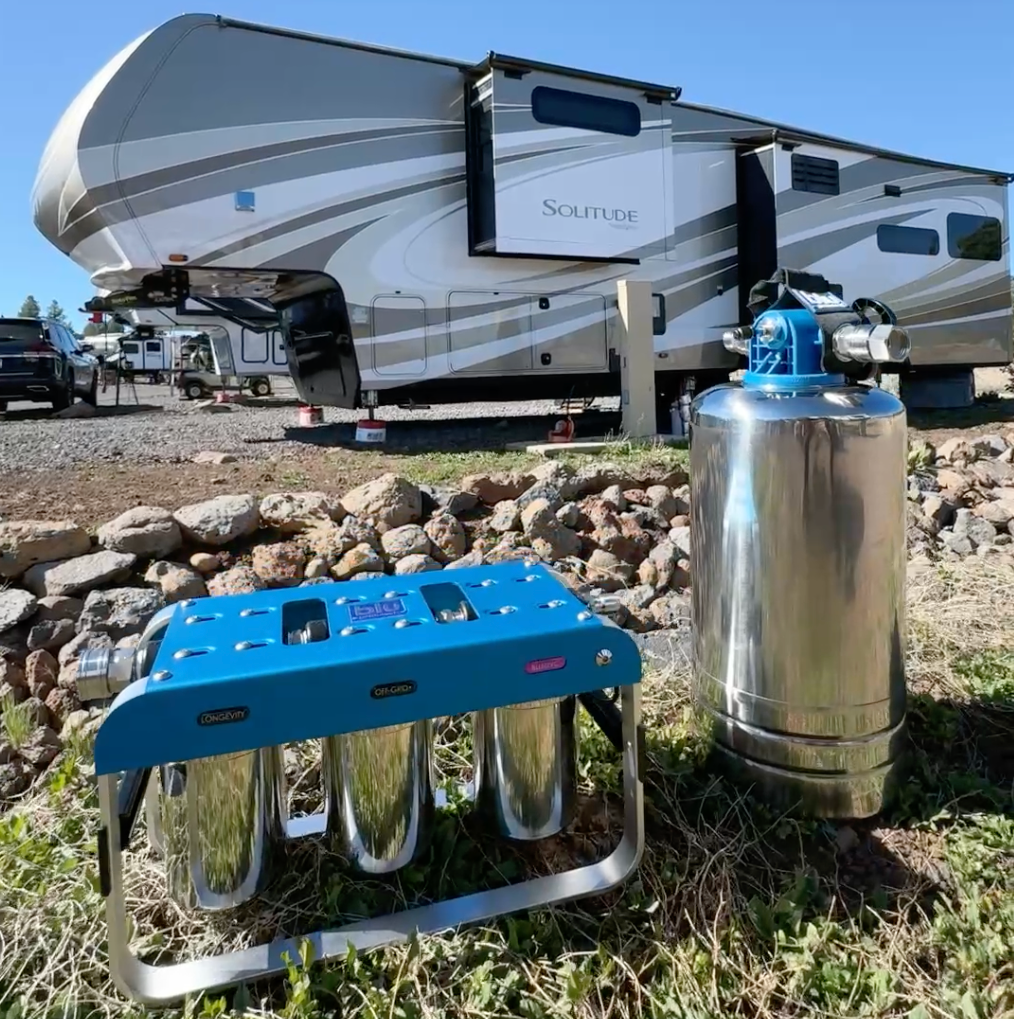 Blue portable stove and propane tank on grass with an RV in the background