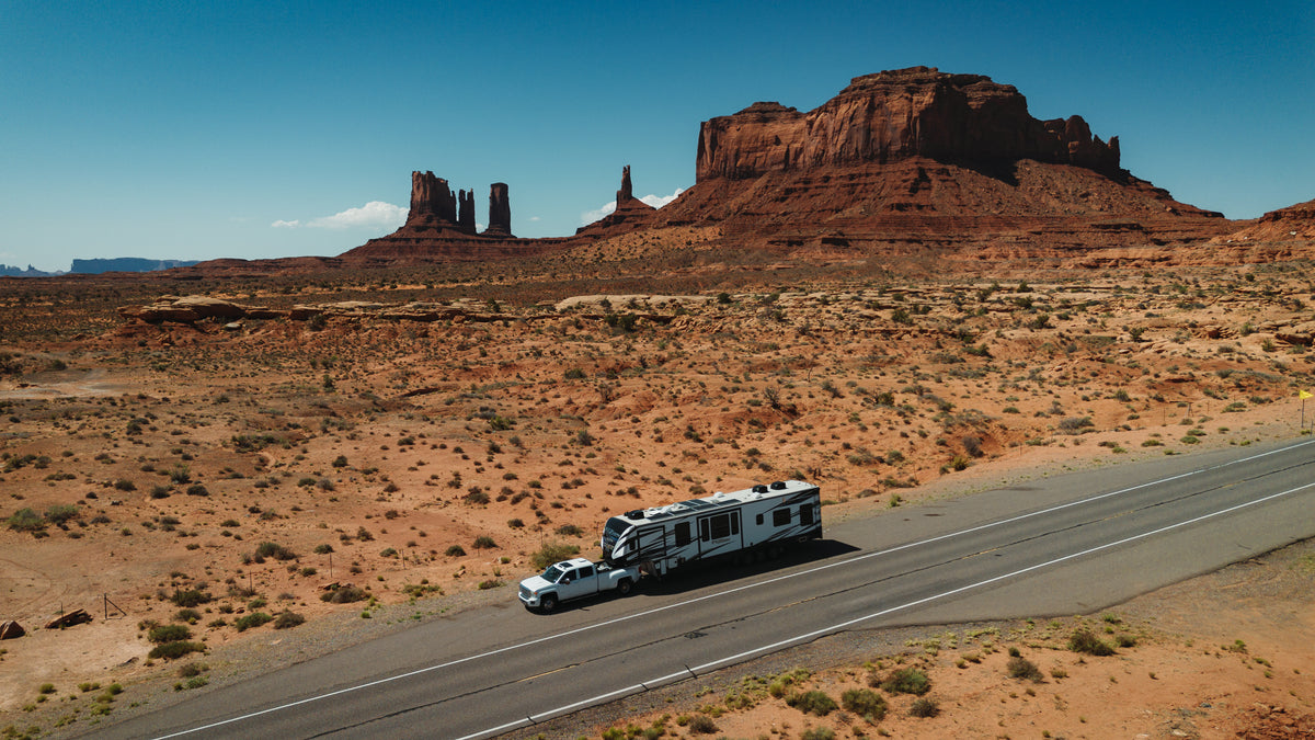 Truck towing a fifth-wheel RV on a desert highway near red rock buttes